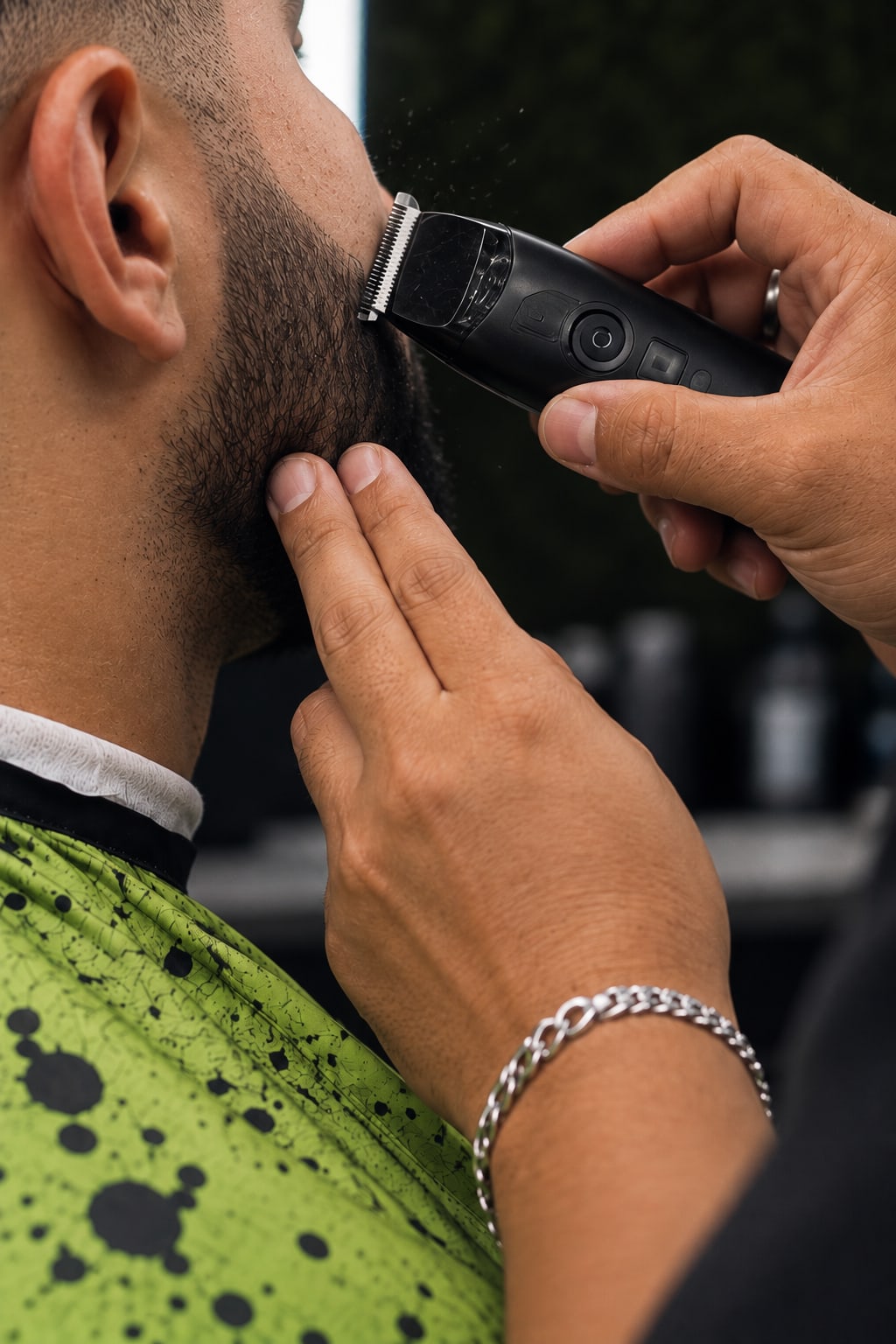 Manos del barbero perfilando la barba de un cliente con la máquina, de cerca